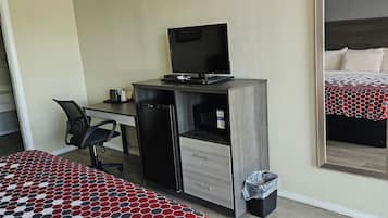A hotel room with a bed, a desk with a computer, a chair, and a large mirror.