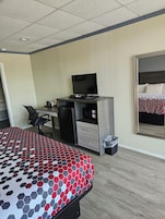 Una habitación de hotel con una cama, un escritorio con computadora, una silla y un espejo grande.