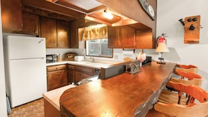 Una cocina con armarios de madera, un refrigerador blanco, una mesa de comedor de madera con sillas y una ventana con cortinas.