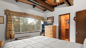 Un dormitorio con una cama grande, un aparador de madera, una ventana con cortinas y una puerta.