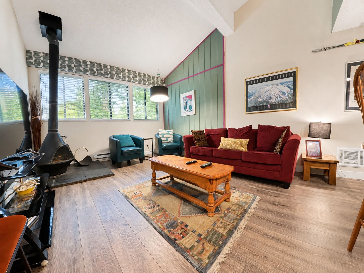 Un salon avec une cheminée, un canapé rouge, une table basse en bois et un tapis à motifs.
