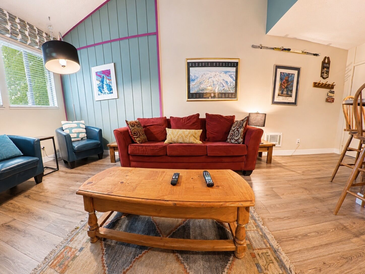A living room with a red sofa, blue armchairs, a wooden coffee table, and a wooden floor.