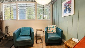 A room with two teal armchairs, a small wooden stool, a table with a tissue box, and a framed picture on the wall.