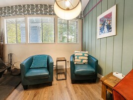 A room with two teal armchairs, a small wooden stool, a table with a tissue box, and a framed picture on the wall.