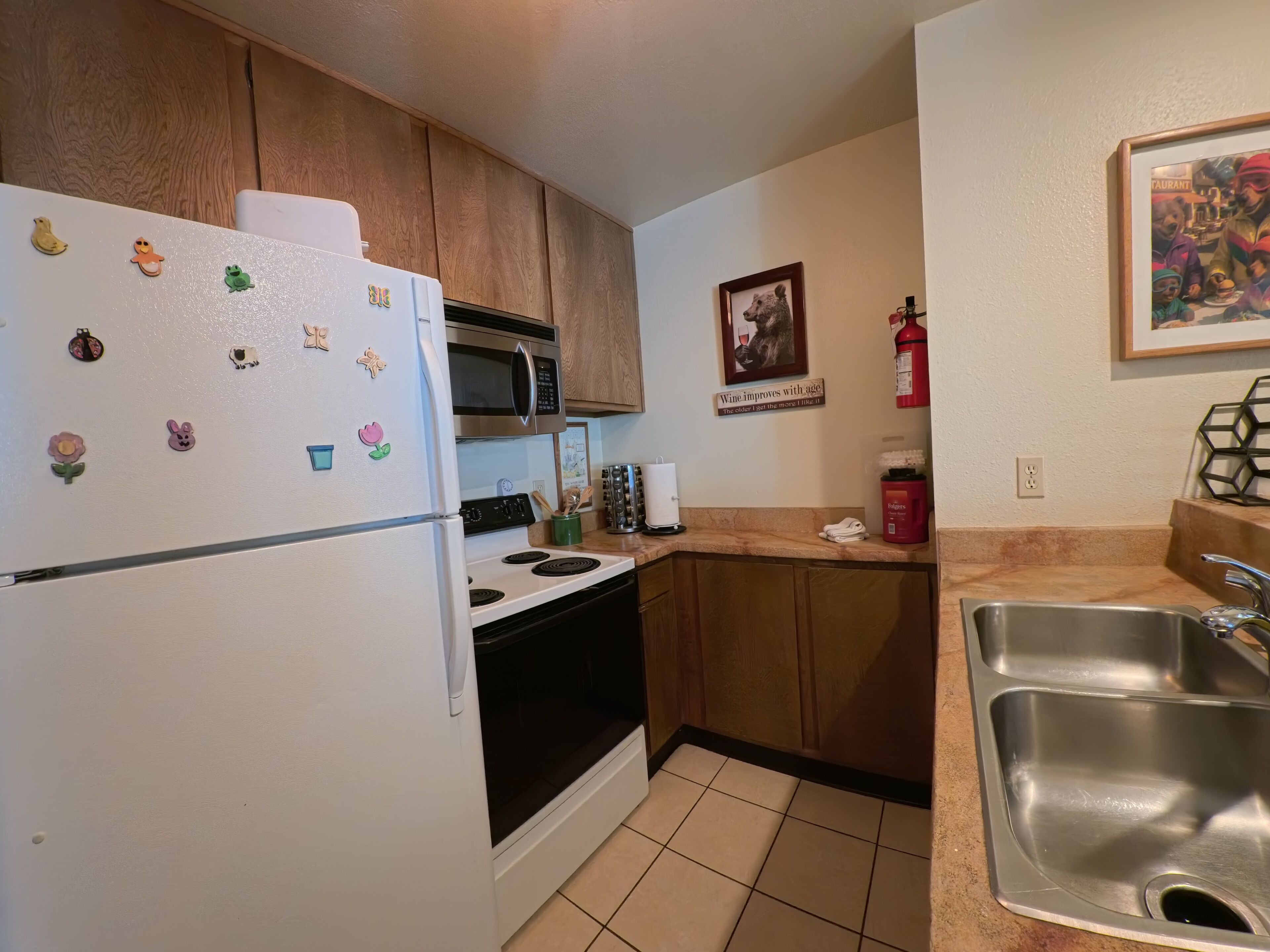 Una cocina con armarios de madera, un refrigerador blanco, un microondas, una estufa y un lavamanos de acero inoxidable.