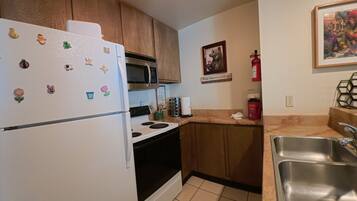 Una cocina con armarios de madera, un refrigerador blanco, un microondas, una estufa y un lavamanos de acero inoxidable.