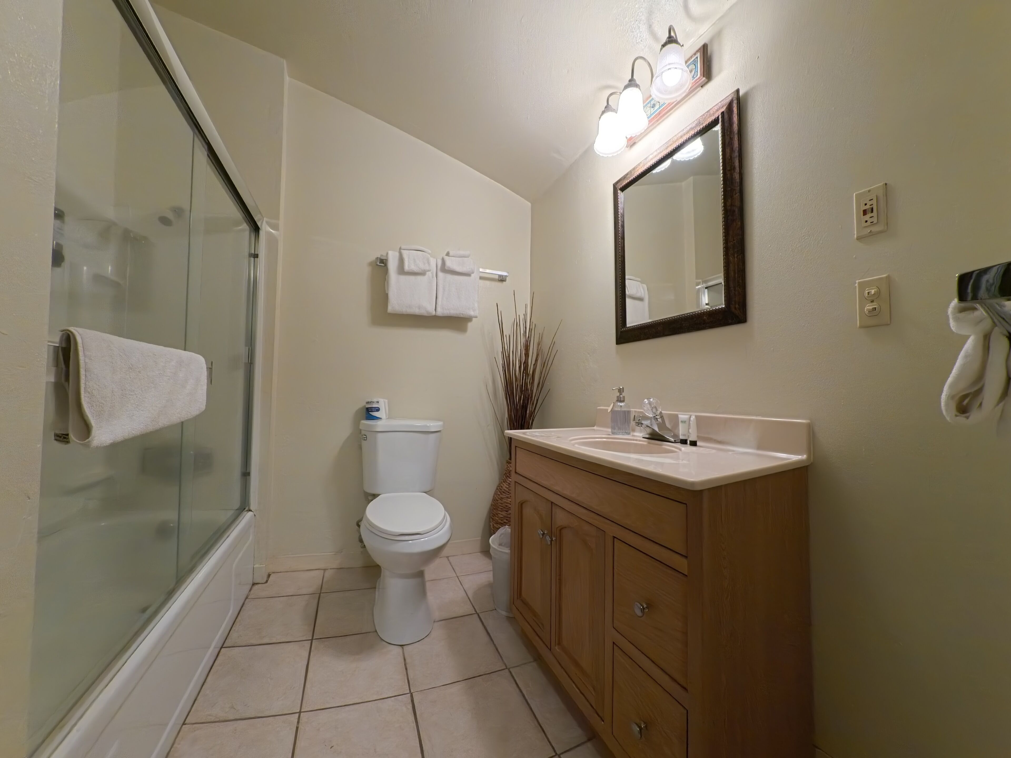 A bathroom with a glass shower enclosure, a toilet, a sink with a mirror, and wooden cabinets.