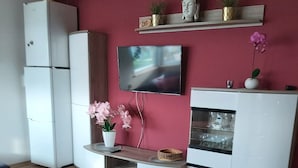 En moderne stue med et fladskærms-tv på væggen, et træspisebord og et indbygget, hvidt tv-møbel med hylder.