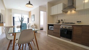A modern kitchen with a glass dining table, wooden chairs, a built-in oven, and a stainless steel range hood. - Artline by Wynwood House (Lima)