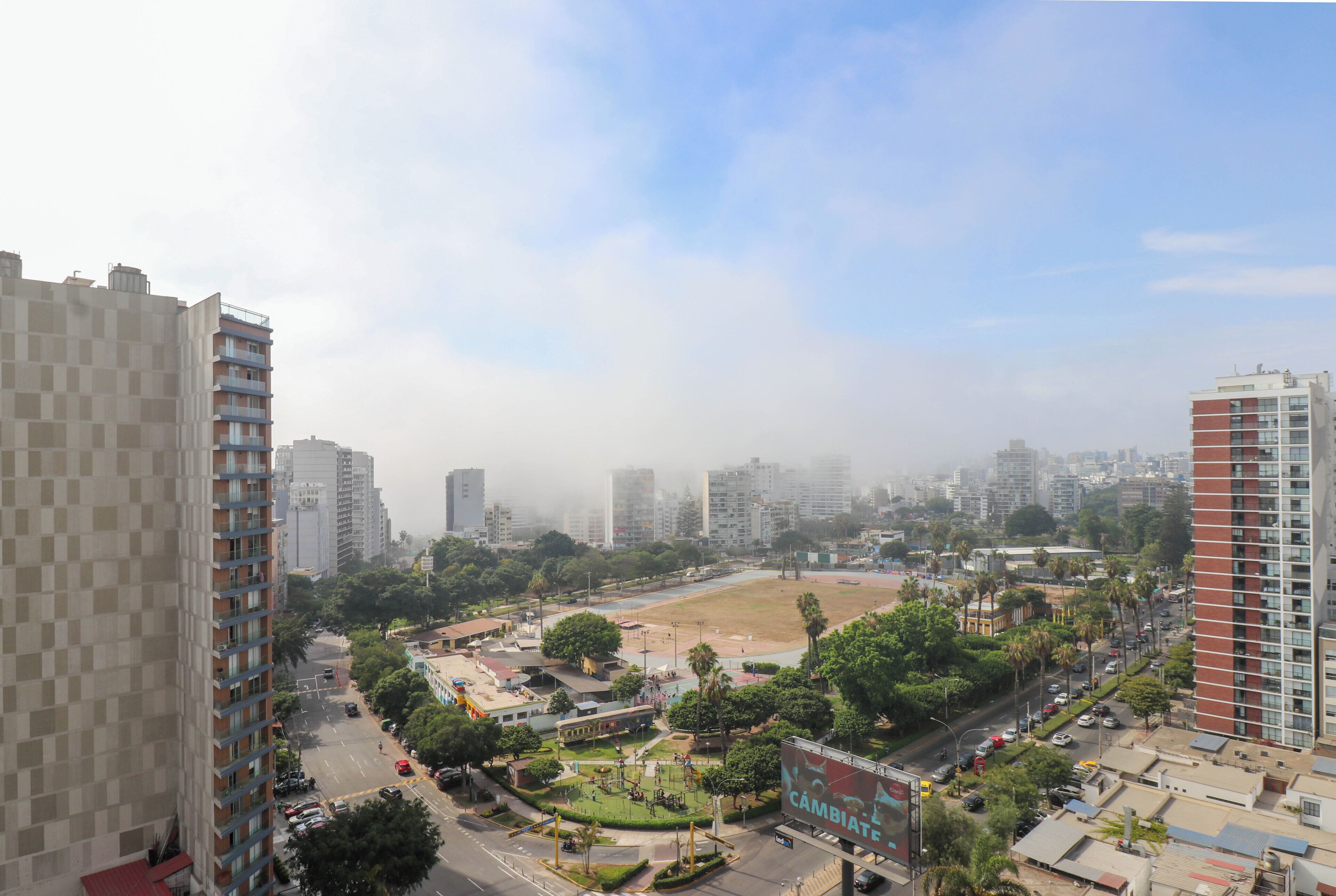 A high-rise building with multiple floors, surrounded by other high-rise buildings and a park area with trees and a playground.