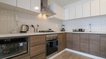 Cocina moderna con armarios de madera, horno empotrado, microondas y cafetera.
