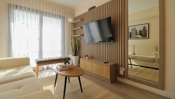 A modern living room with a sofa, a coffee table, a TV mounted on a wooden panel, a potted plant, and a framed picture on the wall. - Artline by Wynwood House (Lima)