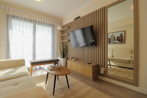 Ein modernes Wohnzimmer mit einer Couch, einem Couchtisch, einem an einer Holzplatte montierten Fernseher, einem Blumentopf und einem gerahmten Bild an der Wand.