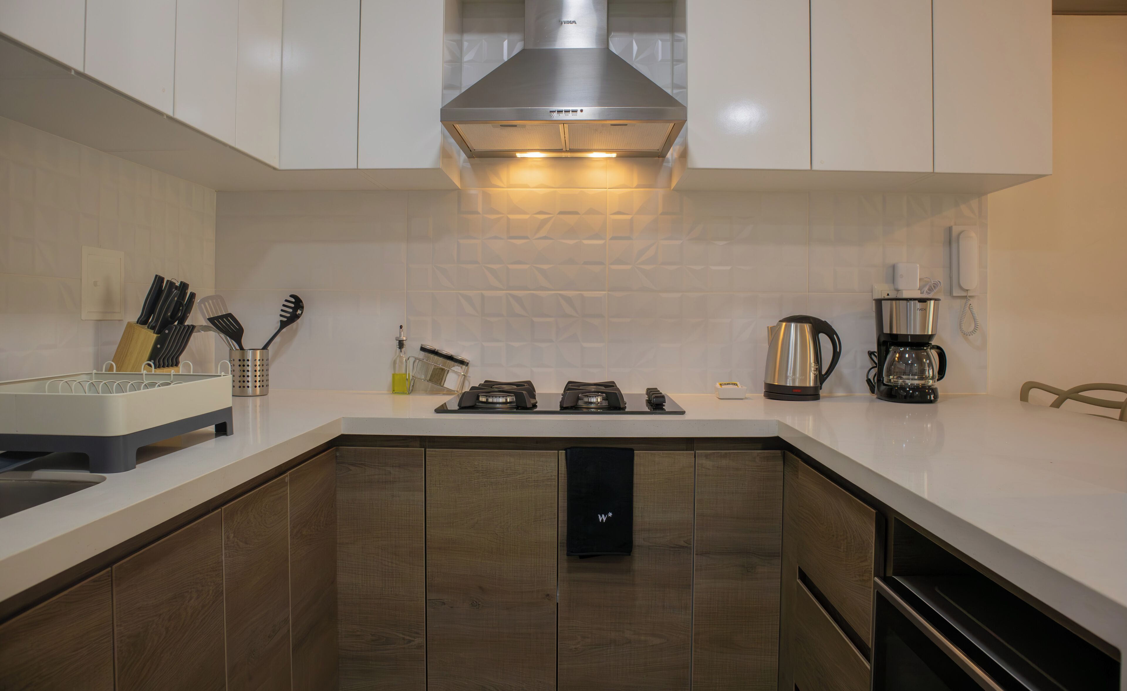 Una cocina moderna con armarios blancos, una campana extractora de acero inoxidable, una cafetera y un hervidor.