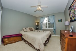 A bedroom with a bed, dresser, window with curtains, and a ceiling fan.