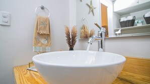 Een wit keramieken wastafel met eenhendelkraan, een houten aanrechtblad en een handdoekrek met een handdoek in strandthema.