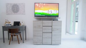 Een moderne kamer met een flatscreen televisie op een kastje, een bureau met een laptop, boeken en decoratieve items.