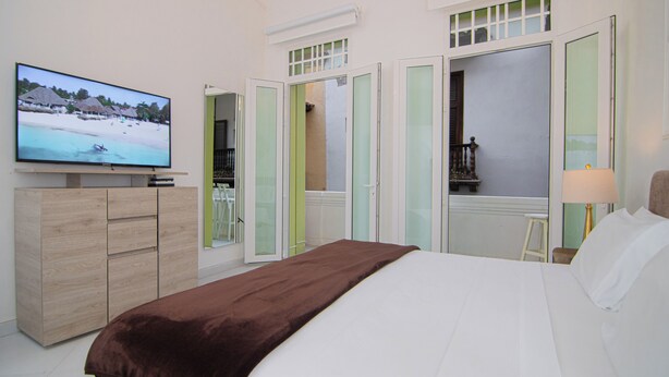 Een hotelkamer met een bed, een televisie, een houten kast en een balkon met uitzicht op het strand.