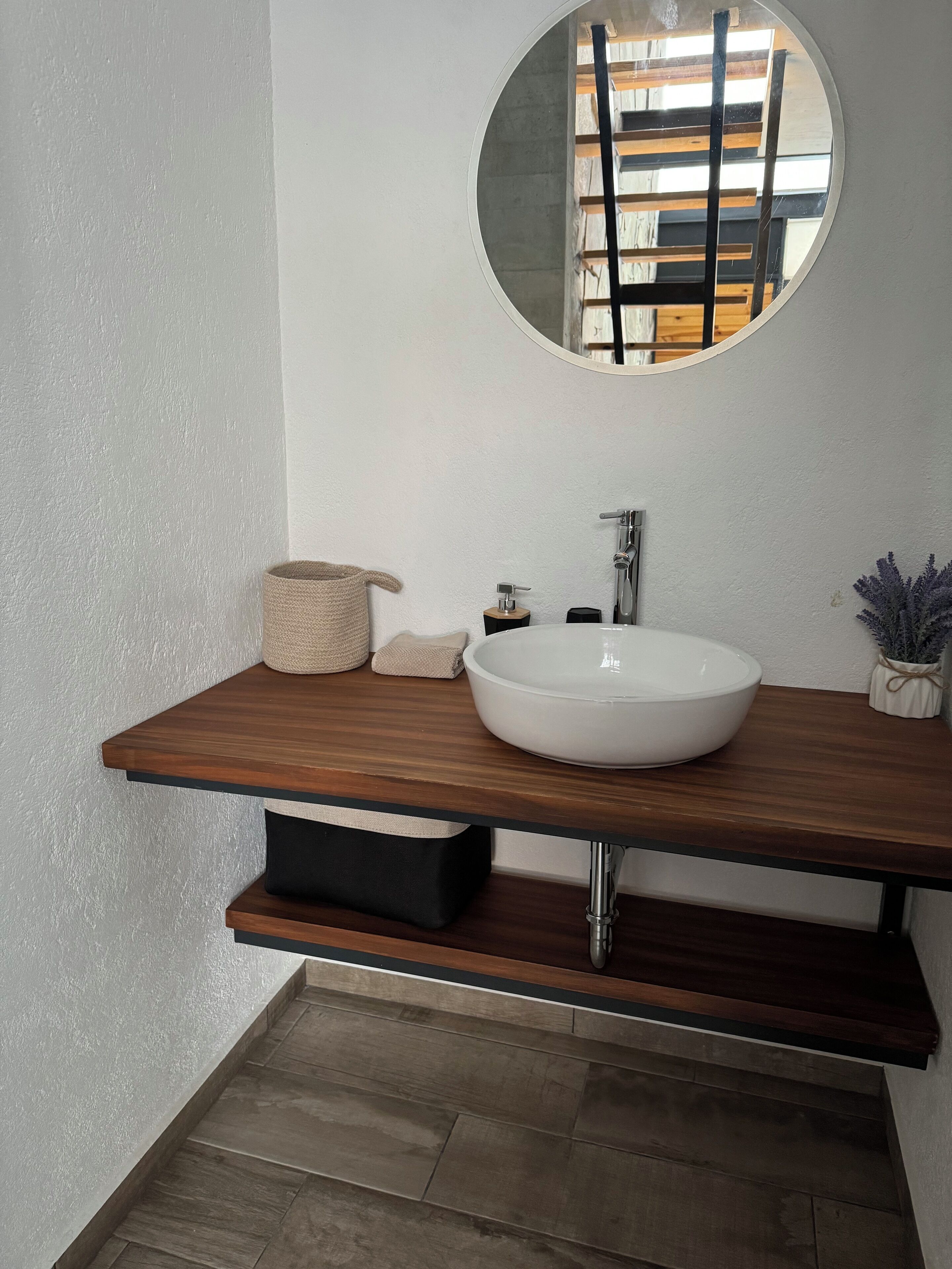 A modern bathroom with a wooden vanity, a round mirror, and a white sink.