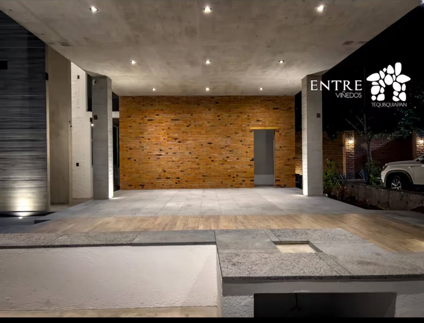 A modern building entrance with a brick wall, concrete pillars, and a car parked outside.