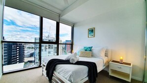 Une chambre à coucher moderne avec une grande fenêtre, un lit, une table de chevet et une commode.