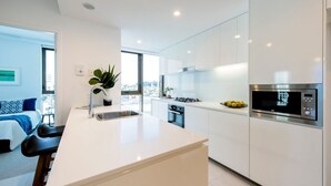 Une cuisine moderne avec des meubles blancs, un îlot central, un four encastré et un four à micro-ondes.