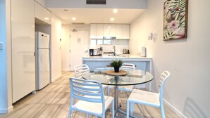 A modern kitchen with white cabinets, a glass dining table, and white chairs. - 2BR Food Drink Hub Pool 2 Cars Gym Rooftop (Brisbane)