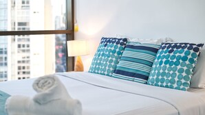 A neatly made bed with blue and white pillows, a rolled white towel, and a lamp on a bedside table. - 2BR Food Drink Hub Pool 2 Cars Gym Rooftop (Brisbane)