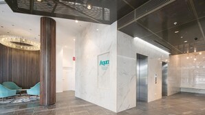 A modern lobby with a marble reception desk, a central elevator, and a seating area with blue chairs. - 2BR Food Drink Hub Pool 2 Cars Gym Rooftop (Brisbane)