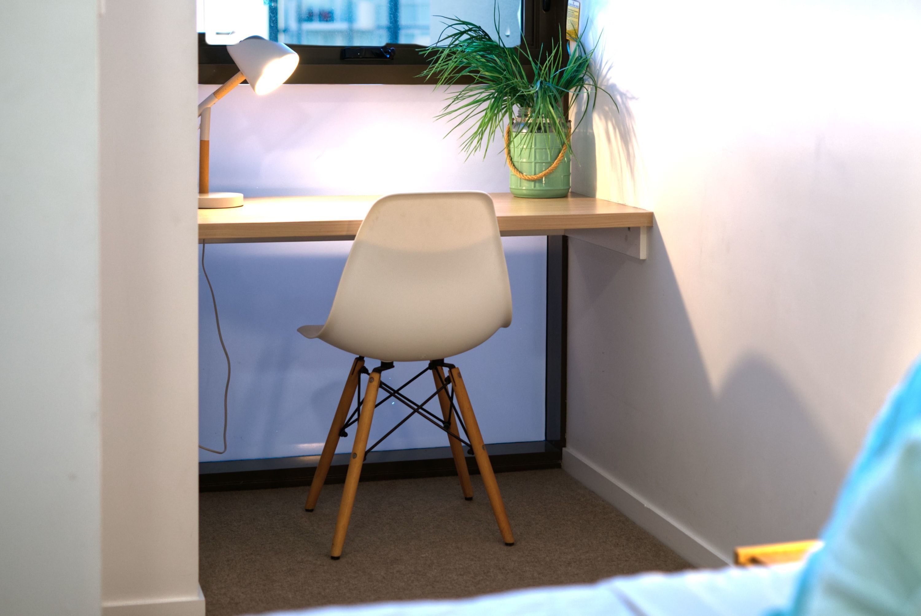 A desk with a lamp, a chair, and a potted plant in a corner of a room.