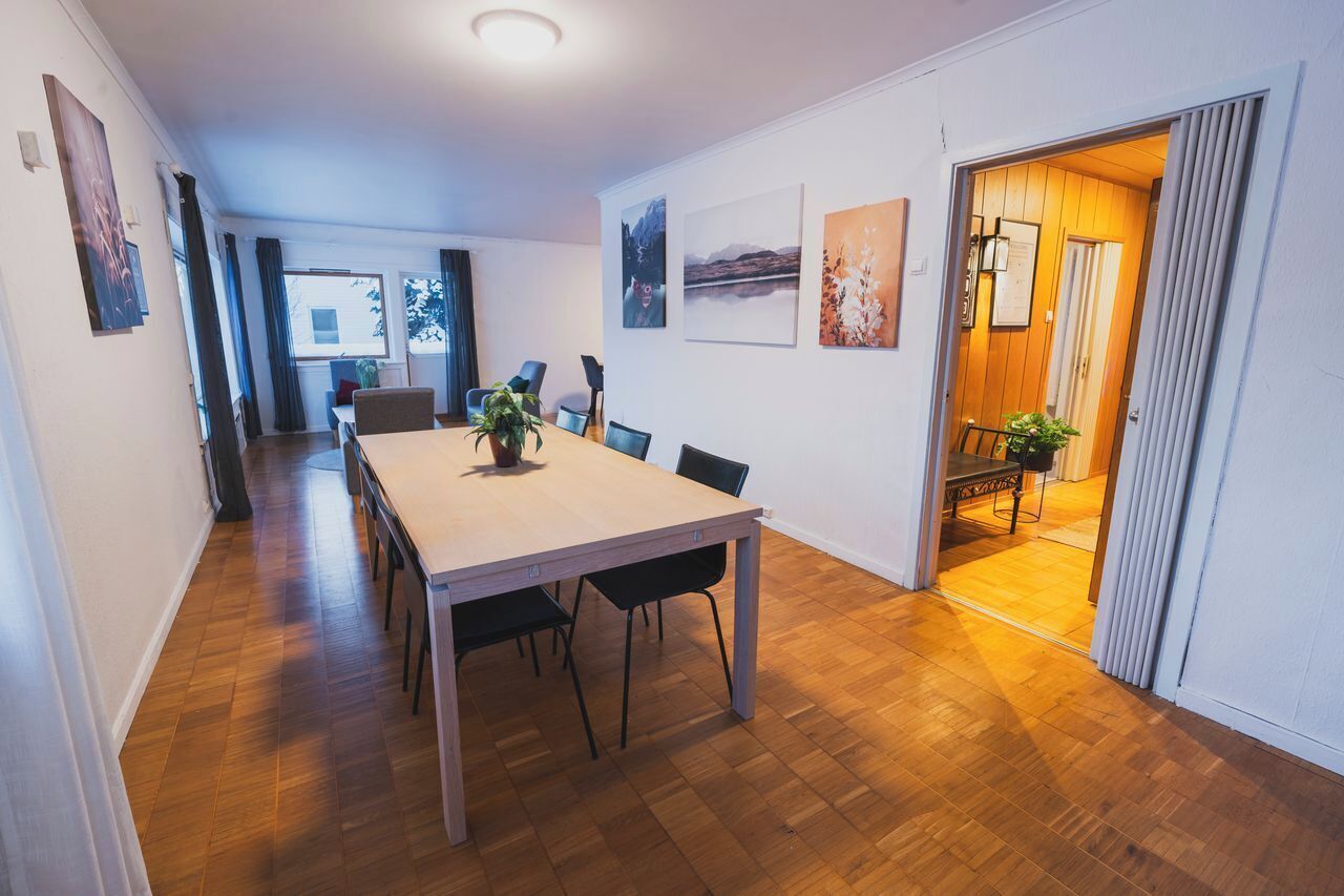 Un comedor con una mesa y sillas de madera, una planta en maceta y obras de arte en las paredes.