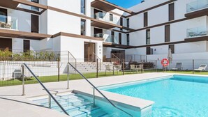 A modern building with a swimming pool, outdoor seating, and a fenced area.
