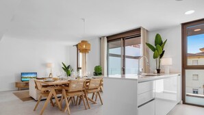 A modern kitchen with a dining area, featuring a large island with a sink and cabinets, wooden chairs, and a hanging light fixture.