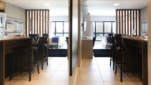 A modern dining area with two long tables, black chairs, and a large window providing natural light. - Studio Shopping OKA Floripa - SOK132 (Florianopolis)