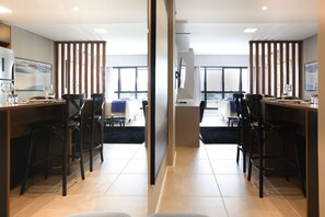 Un espace repas moderne avec deux longues tables, des chaises noires et une grande fenêtre qui laisse entrer la lumière naturelle.