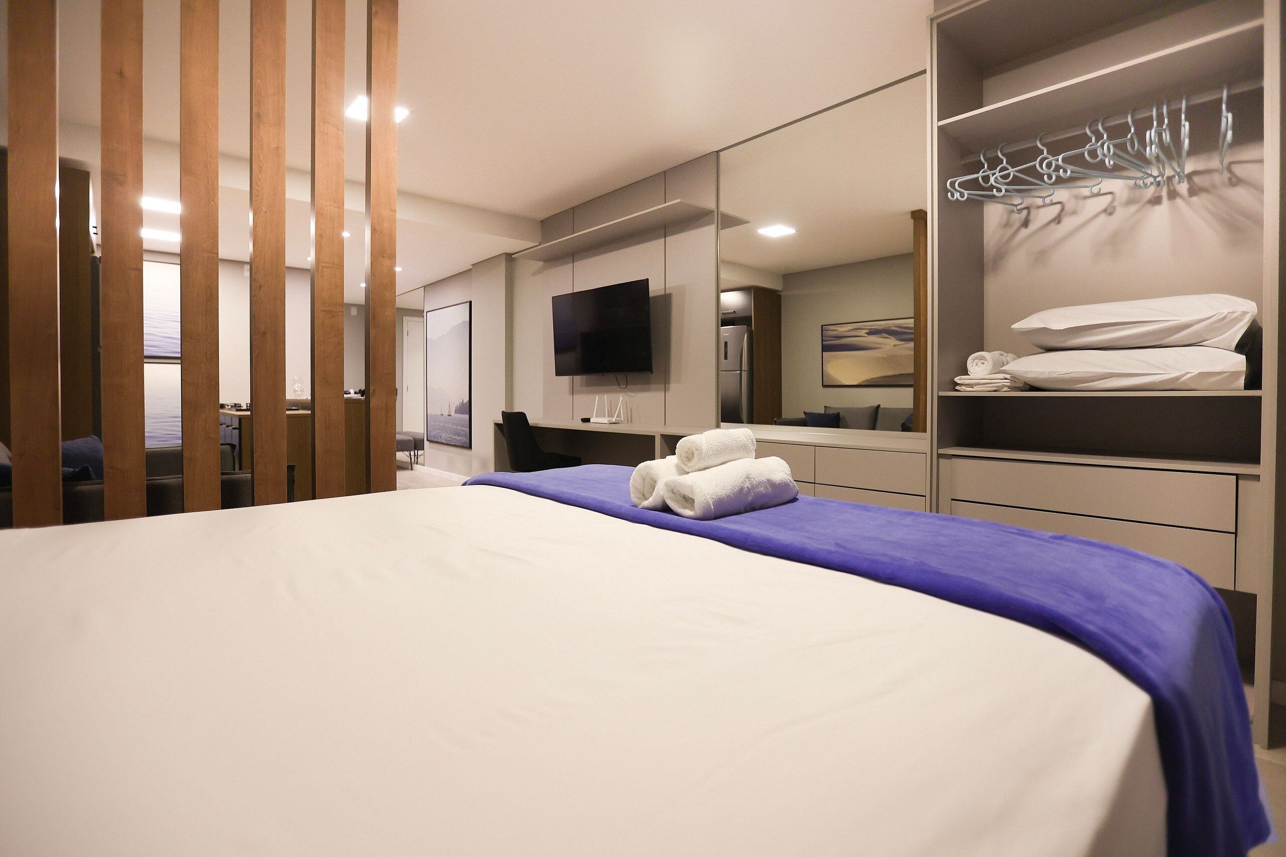 Una habitación de hotel moderna con una cama grande, un televisor de pantalla plana, un armario con espacio para colgar y un espejo.