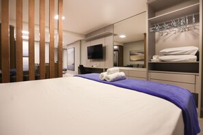 Una habitación de hotel moderna con una cama grande, un televisor de pantalla plana, un armario con espacio para colgar y un espejo.
