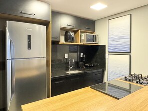 Una cocina moderna con un refrigerador de acero inoxidable, armarios negros, una encimera de madera y una estufa a gas.
