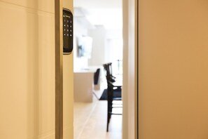 A hallway with a digital keypad door lock, leading to a dining area with a table and chairs.