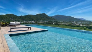 A clear blue pool with a wooden deck and lounge chairs, surrounded by lush greenery and mountains in the background. - Studio Shopping OKA Floripa - SOK132 (Florianopolis)