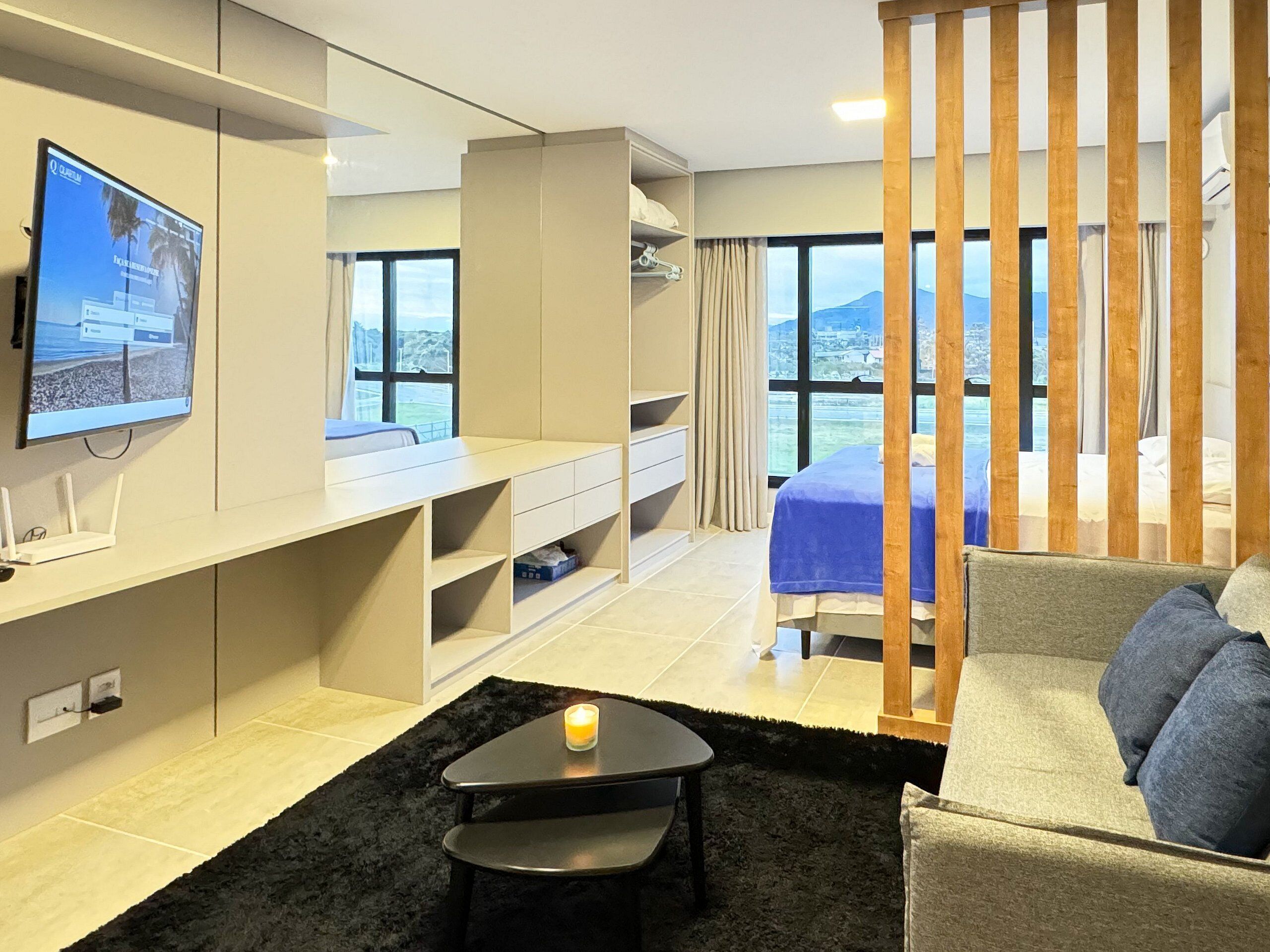 Una habitación de hotel moderna con un televisor grande, un escritorio, un sofá cómodo y un balcón con vistas a las montañas.
