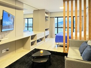 Una habitación de hotel moderna con un televisor grande, un escritorio, un sofá cómodo y un balcón con vistas a las montañas.