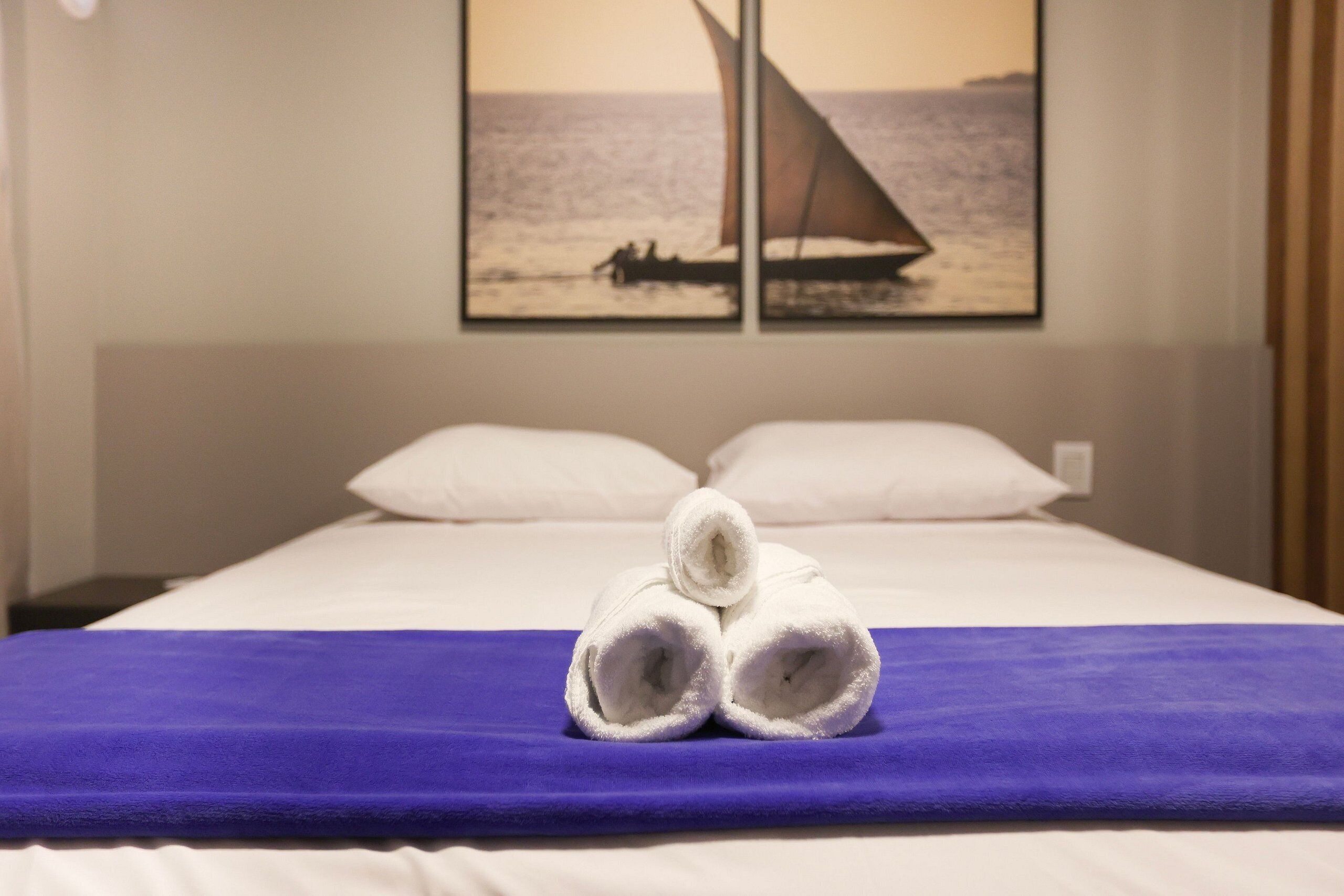 Un lit avec des draps blancs, une couverture violette et une paire de serviettes enroulées posées sur le lit.