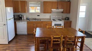 A kitchen with wooden cabinets, a white stove, a sink, and a dining table with chairs. - Candle Lake Golf Course - Spruce Cabin (Candle Lake)