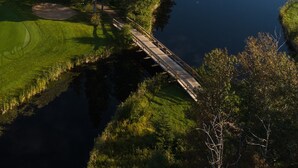 Un parcours de golf avec un étang, un pont en bois et une zone boisée.