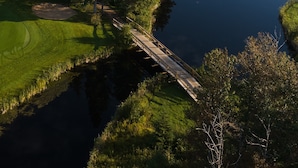 Un campo de golf con un estanque, un puente de madera y una zona boscosa.