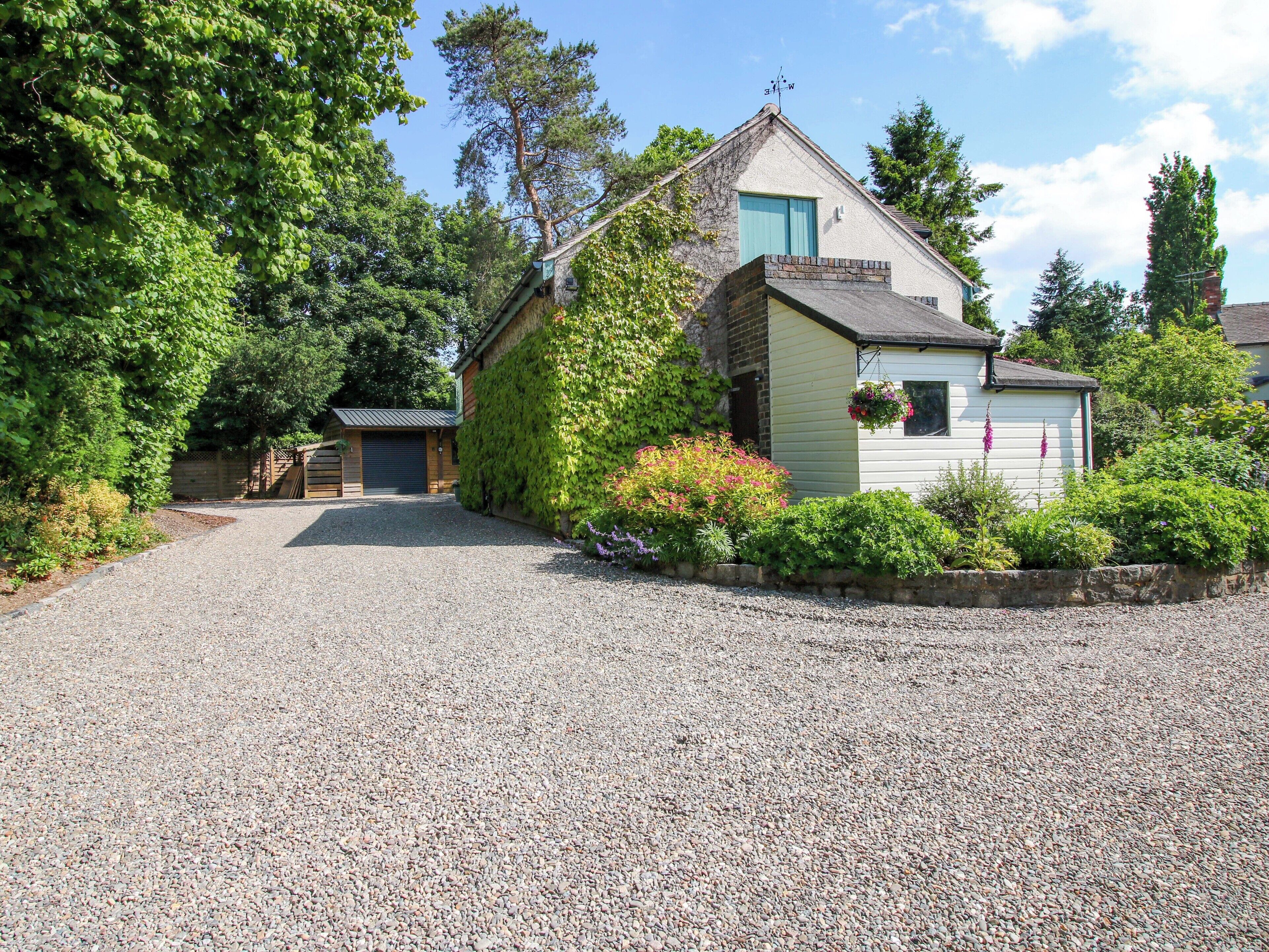 Une maison avec une allée en gravier, un garage et un petit jardin agrémenté de fleurs et d’arbustes.
