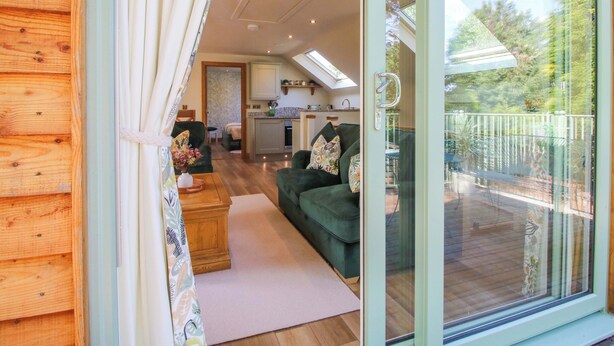 Una sala de estar acogedora con un sofá verde, una mesa de centro de madera y vistas a un balcón con terraza de madera.