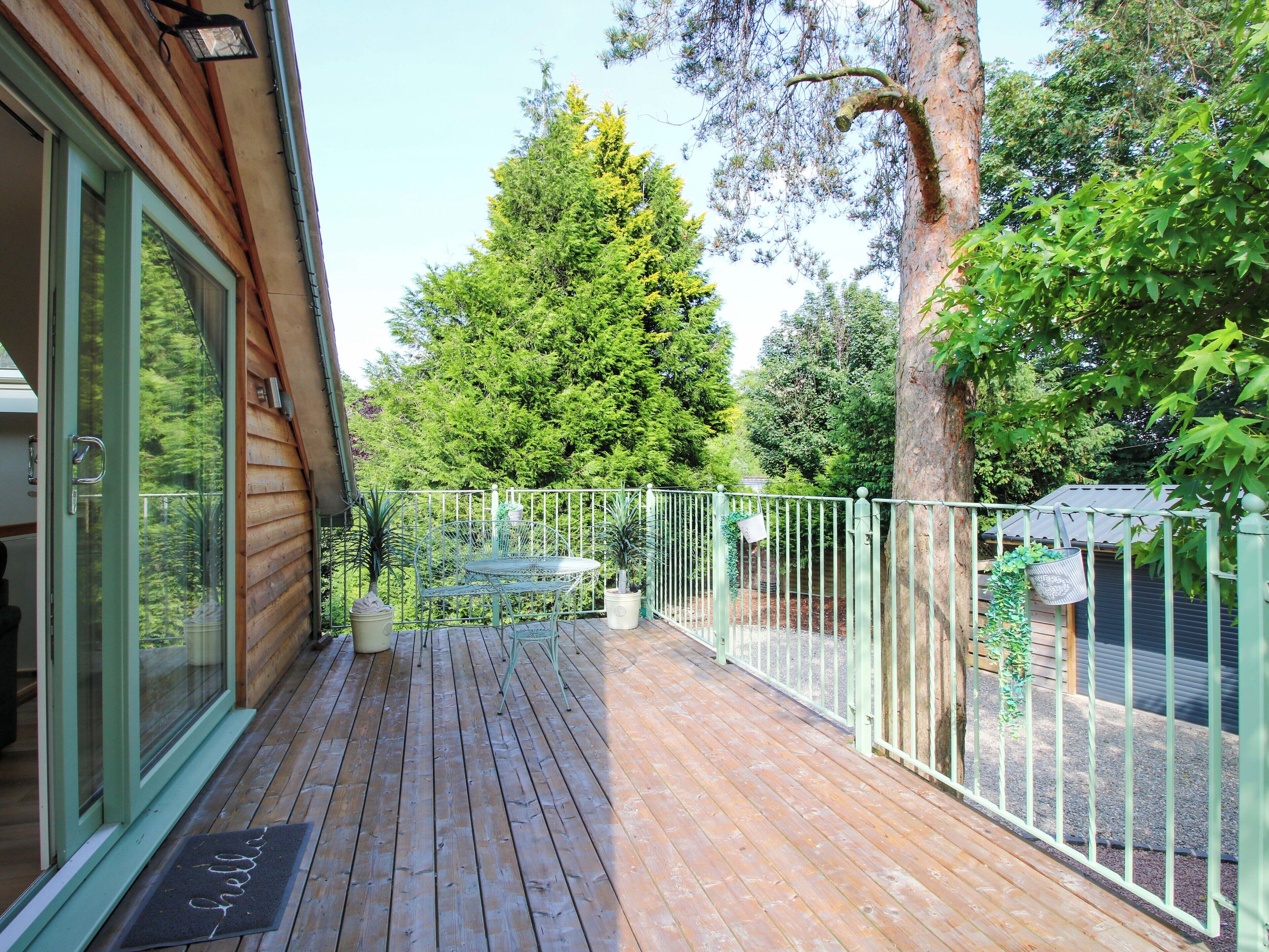 Une terrasse en bois avec une rambarde en métal, des plantes en pot et une vue sur des arbres et un bâtiment.