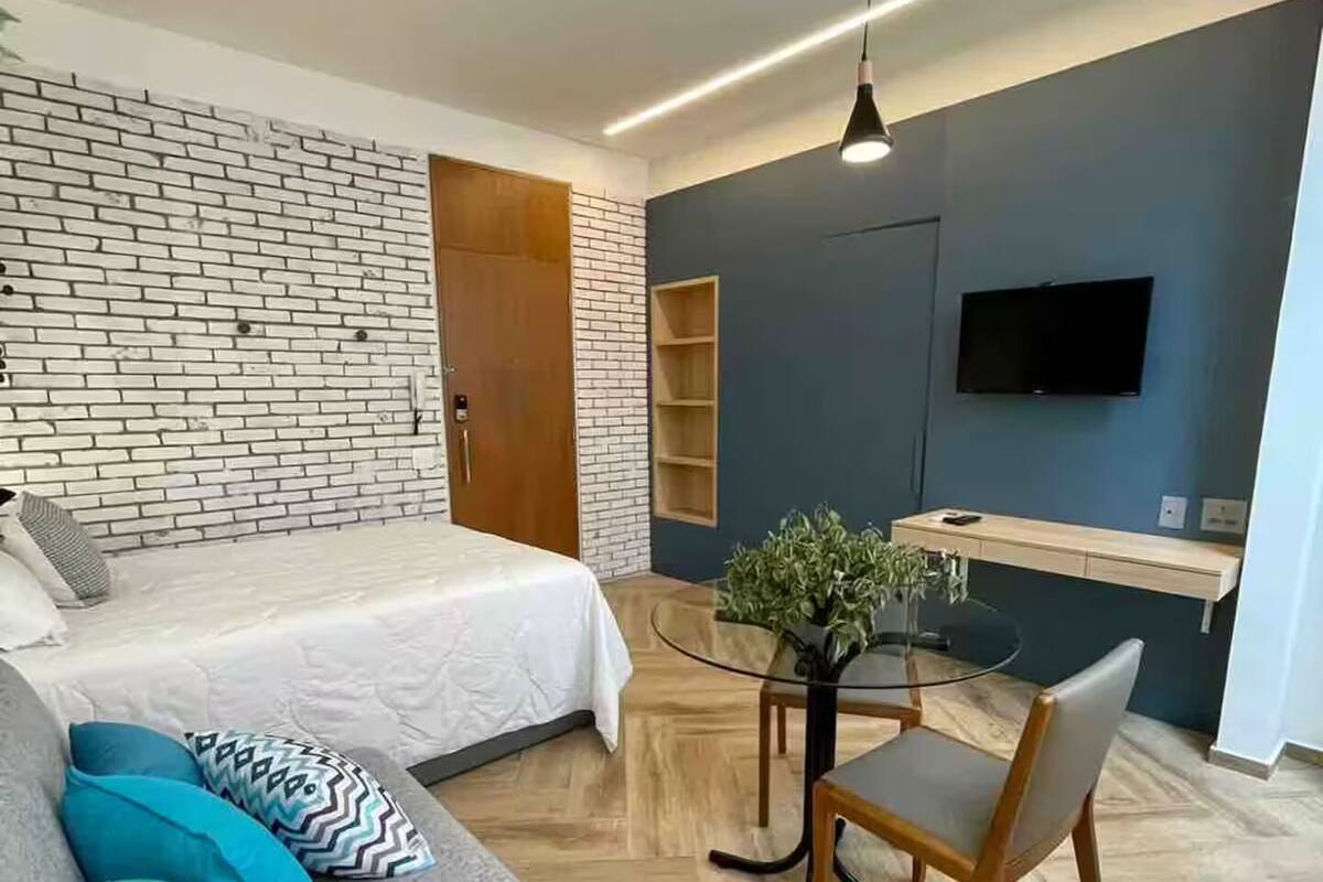 Un dormitorio moderno con pared de ladrillo, cama, sofá, escritorio y televisor.